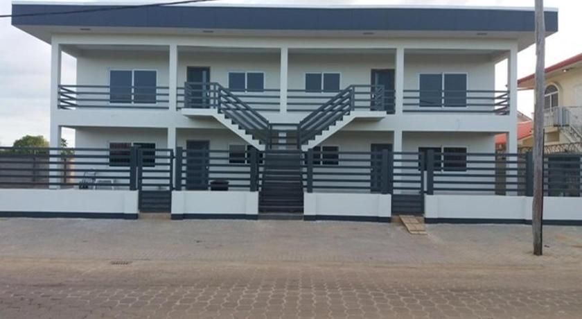 The white two-storey HOMI Paramaribo apartment building with dark grey balconies and a central staircase, seen from the street